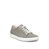 A low-top sneaker in a muted sage green color, featuring white laces, a thick white sole, and a small tan brand tag on the side, set against a plain white background.
